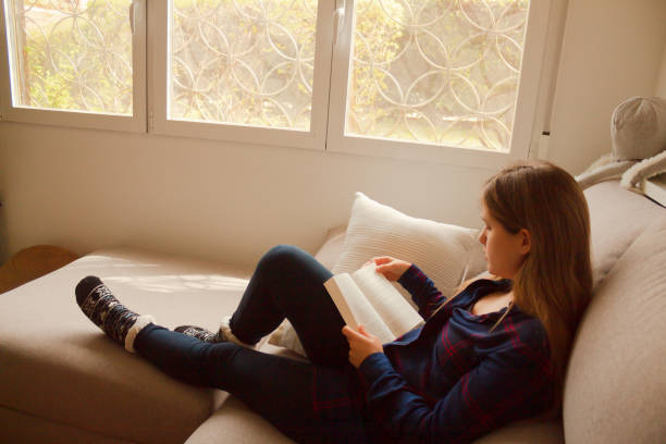 istock Blonde European female reading a book on a comfortable cream sofa 1459916438