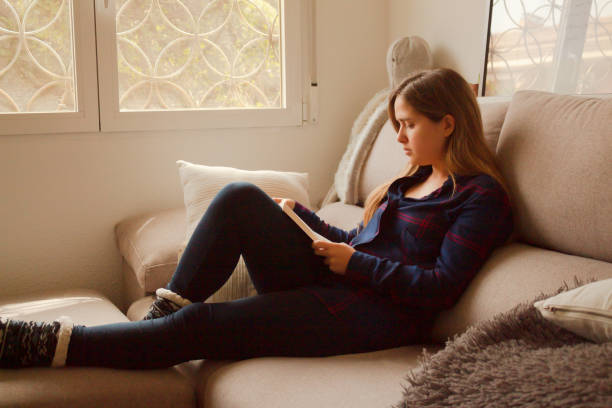 istock Blonde European female reading a book on a comfortable cream sofa 1459916462