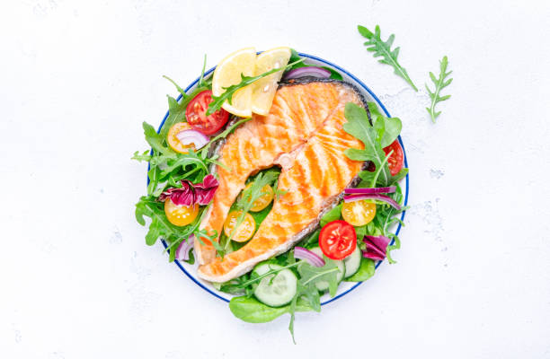 istock Grilled salmon steak with vegetables, tomatoes, arugula and lettuce side dish salad on plate, gourmet lunch. White table background, top view 1459916540
