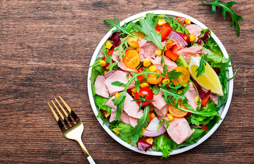 Fresh tuna vegetables salad with colorful cherry tomatoes, red onion, sweet corn, paprika, lettuce, radicchio and arugula. Rustic wood table background, top view