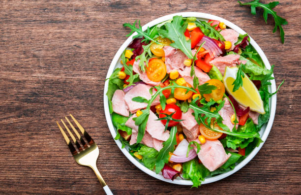 Fresh tuna vegetables salad with colorful cherry tomatoes, red onion, sweet corn, paprika, lettuce, radicchio and arugula. Rustic wood table background, top view stock photo