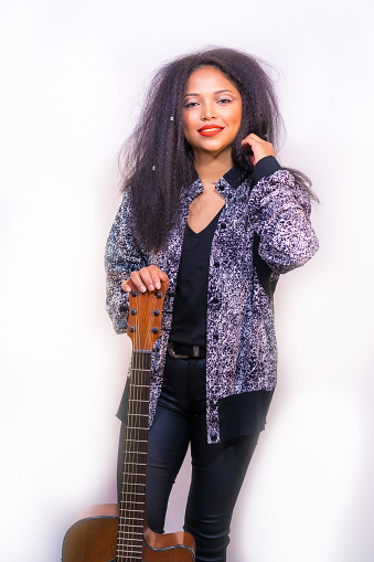 A vertical portrait of a stylish pretty female musician holding an acoustic guitar posing in a studio