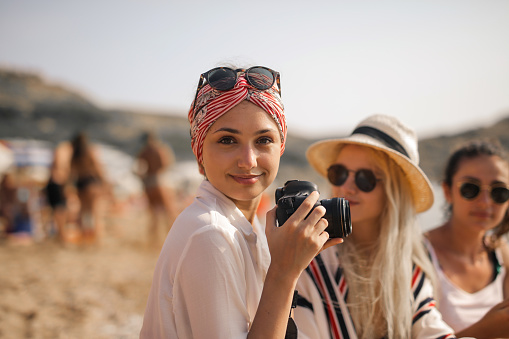 A young caucasian lady with a white t-shirt a camera smiling on a beach