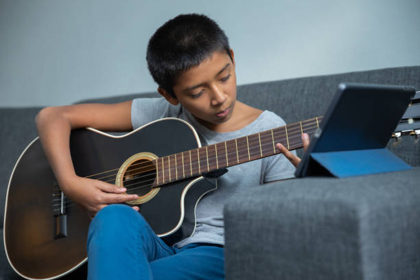 istock Boy sitting on the sofa and having online guitar lessons - new normal 1459919215