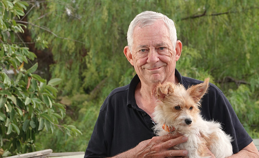 A closeup of a smiling elderly man holding a wire-haired terrier in the park