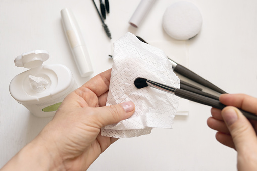 Cleaning makeup brushes with special disinfecting cloth. Hand holds the tool and wipes it.