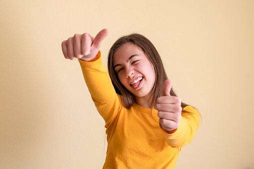 An excited young girl with thumbs up on a yellow wall background