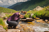 woman drinks water from a mountain spring, sitting, a clear river in the mountains on a sunny day