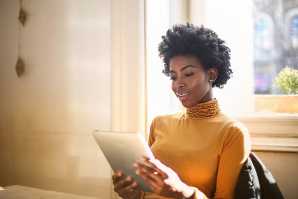 istock Beautiful black female looking at her tablet while sitting by the window 1459921675
