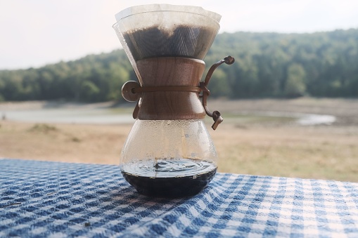 Chemex coffeemaker cup on a checkered tablecloth with a forest in the background