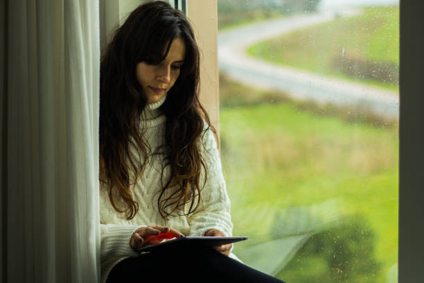 istock Caucasian female sitting on a windowsill and using a tablet 1459922358