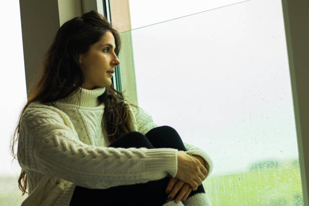 istock Caucasian female sitting on windowsill and looking out the window 1459922511