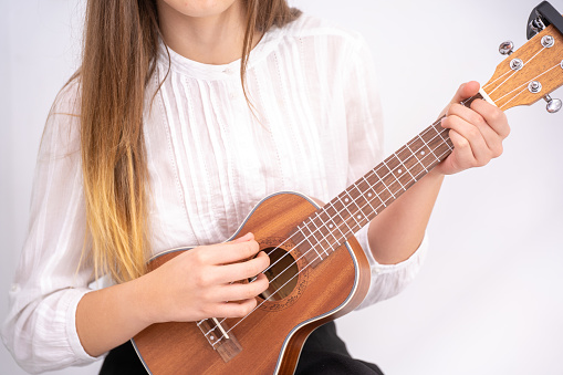 A young lady with an ombre hairstyle playing the ukulele wearing a white blouse