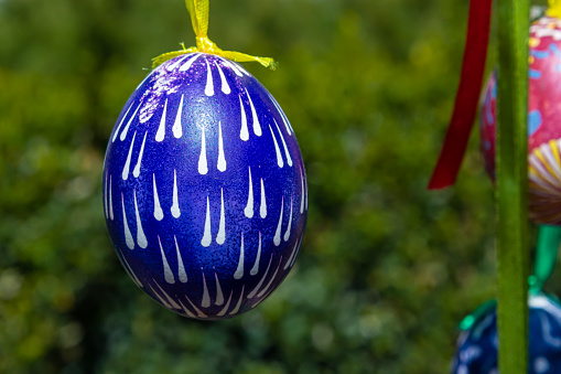Painted eggs hang from the branches of the Easter tree. The focus is on a yellow egg painted by children by hand. High quality photo