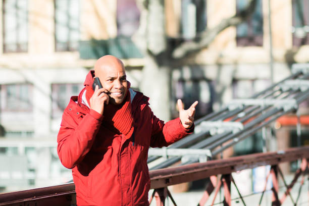A bald Latin male talking on his phone while walking in the street