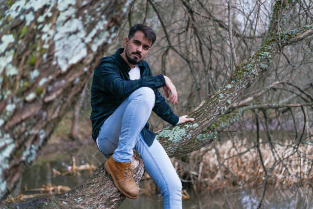 A young Latin male posing on a leafless tree trunk in the autumn park