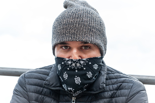 A closeup portrait of a young male wearing winter clothes with his face half-covered with a scarf staring at the camera