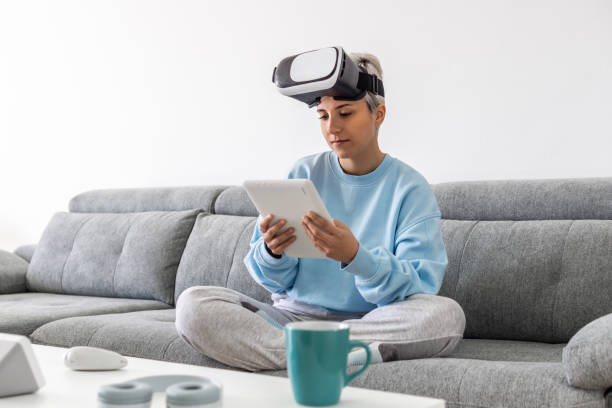 istock Adult woman using a VR headset and a tablet while sitting on a sofa 1459926189