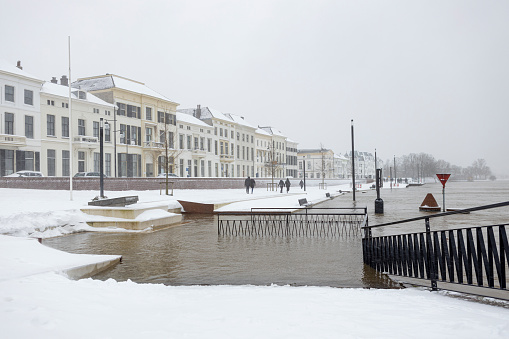 Zutphen, Netherlands – February 08, 2021: Snowy white picturesque view of cityscape historic facades at IJsselkade boulevard during high water level and snowstorm
