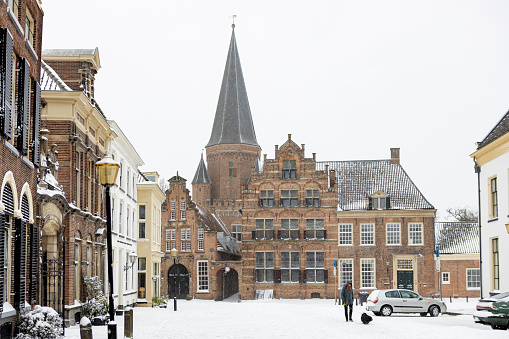 Zutphen, Netherlands – February 08, 2021: Snow in the streets of historic  medieval city center during a snowstorm with people passing the Bolwerck cultural center and Drogenapstoren behind