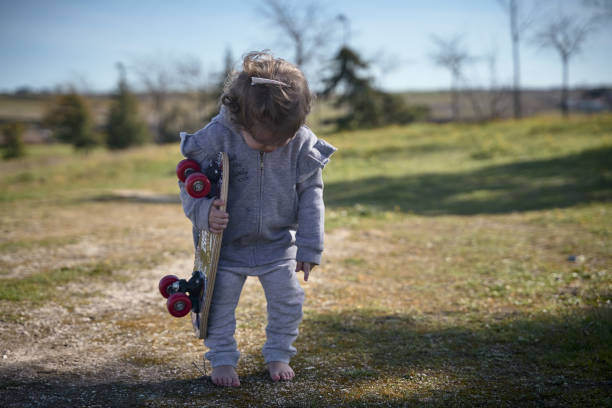 istock Cute kid standing barefoot on the grass while holding a skateboard in the park 1459928020