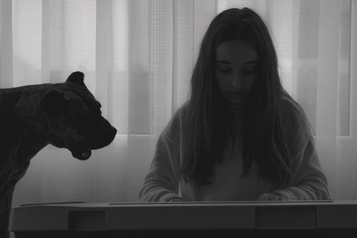 A grayscale shot of a dog and a Spanish female playing on a digital piano