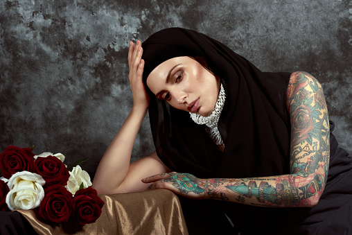 Artistic studio portrait with red roses and white flowers of the ecstasy of a contemporary tattoed nun