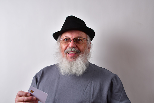 An American man with glasses and hat holding a plastic card with a chip on a white wall background
