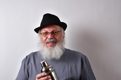An American man with glasses and hat holding an aluminum shaker on a white wall background