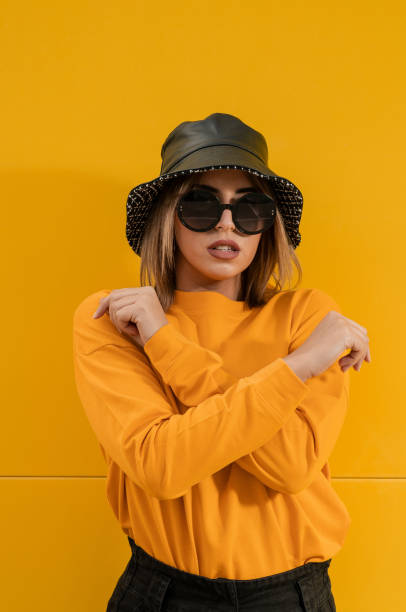 istock Young lady with sunglasses and hat posing for the camera on a yellow background 1459930287