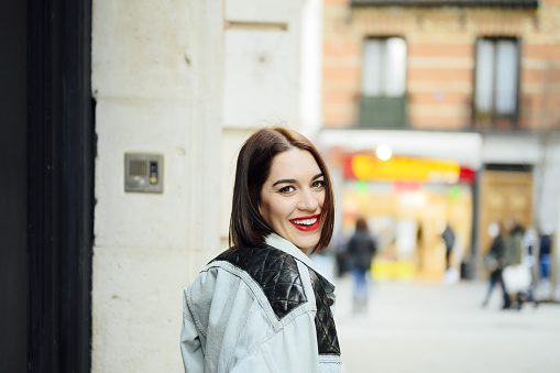A happy beautiful Spanish girl with a bob style haircut and red lipstick posing on the street