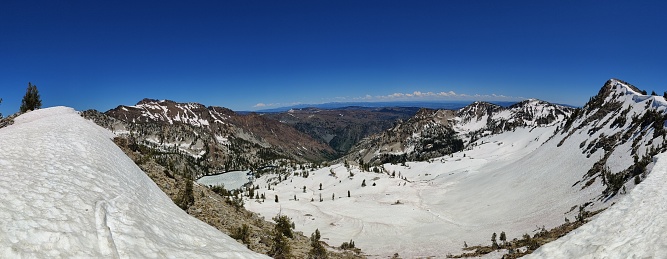 A panoramic of a snow-covered valley surrounded by mountains with sparse vegetation under the blue sky