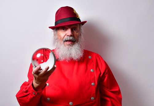 A retired American male with a red bib shirt and fedora hat thoughtfully examining a crystal ball