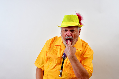 A senior male in a yellow outfit doing a gagging pose in front of a white wall