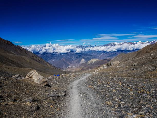 istock Rocky mountain trail looking at the peaks of a mountain range covered by fluffy clouds 1459936368