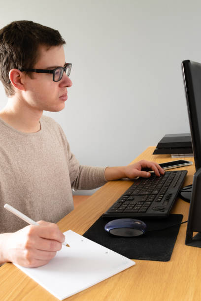 istock Vertical shot of a Spanish Caucasian male using his computer and taking notes indoors 1459936383