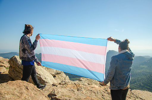 Picture of Transgender Activist Men in back view Showing with proud LGTB Blue and Pink Trans Flag at the Mountain Cliff