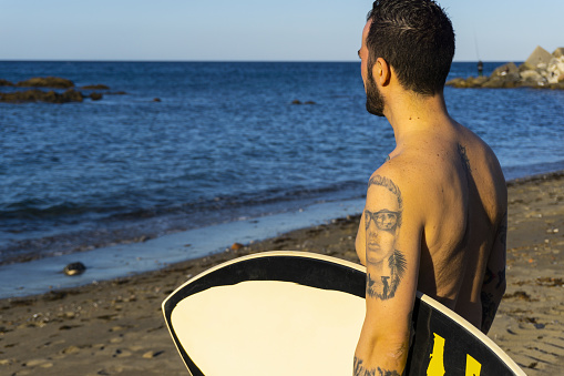 A closeup shot of a Caucasian young male surfer standing on the beach