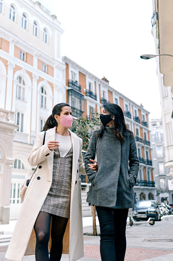 Two happy women talking and walking in the street with their face masks on.