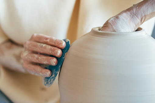 Close up, woman's hands making ceramic vase on potter's wheel