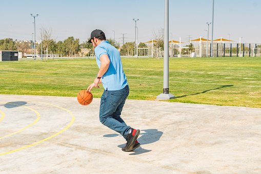 Vista trasera de un hombre caucásico jugando baloncesto al aire libre, en un parque deportivo público photo
