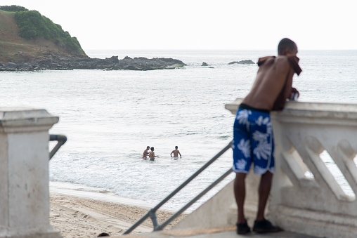 Salvador, Brazil – February 10, 2018: Salvador, Bahia, Brazil - February 09, 2018: Man watches the sea from Farol da Barra beach after Carnival night in Salvador, Bahia.