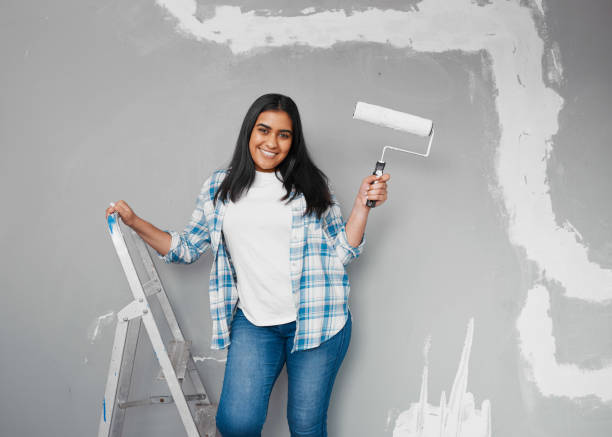 istock Young Indian woman poses with paintbrush roller getting ready to paint wall 1459944318