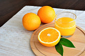 orange juice in drinking glass on cutting board isolated with oranges on kitchen table