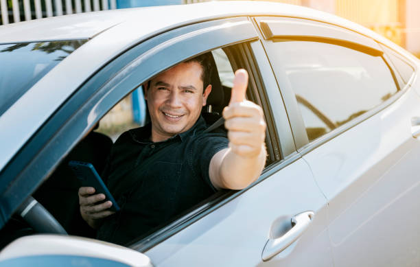 istock Smiling driver holding cellphone showing thumb up. Driver man showing thumb up while holding cellphone. Happy driver giving a thumbs up on the road. safe driving concept 1459948181