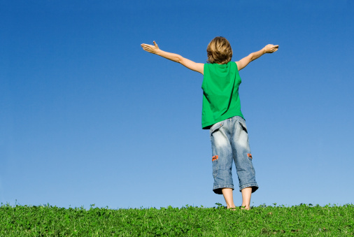 child outdoors with arms raised in joy