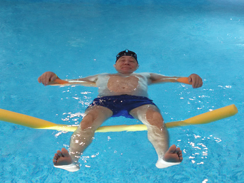smiling man lies on the water in the pool on swimming noodles close-up