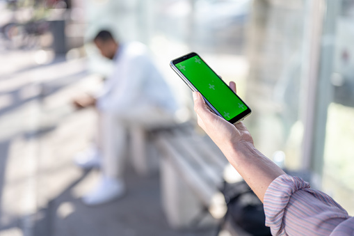 Close-up of woman's hand using smartphone with green screen.