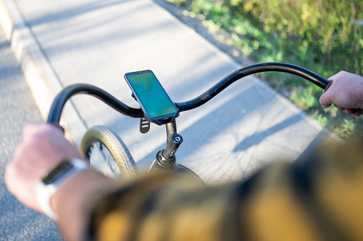 Elevated view of smartphone on handlebar of bicycle on asphalt road.
