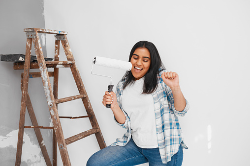 Close up shot of young woman singing and dancing while painting wall home DIY. High quality photo